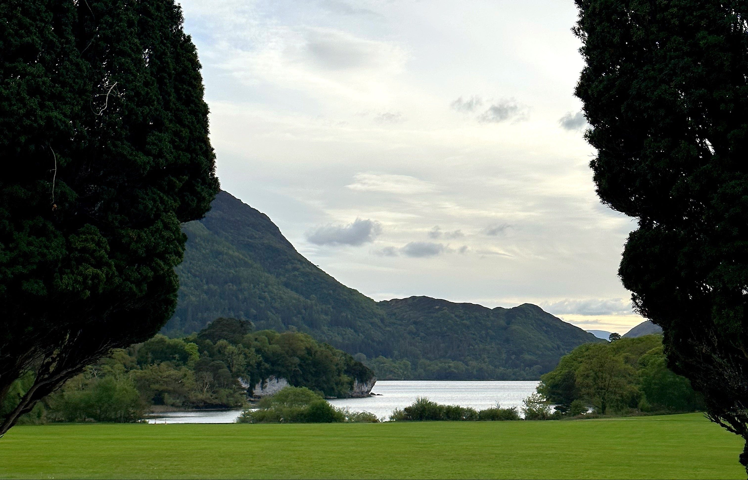 Landscape with a lake, mountains, and trees under a cloudy sky.